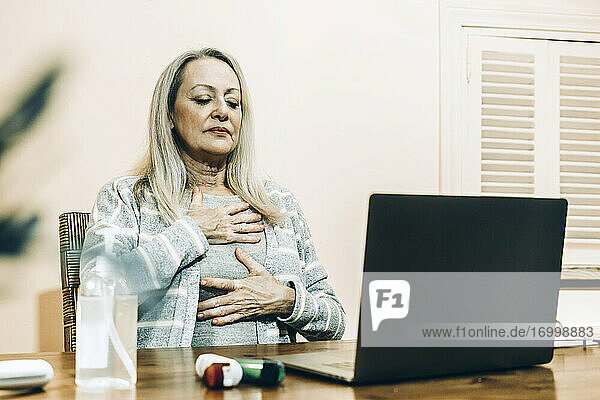 Senior woman doing breathing exercise during online consultation at home
