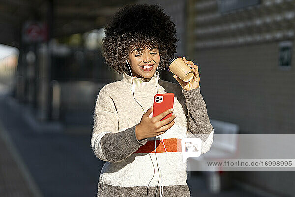 Lächelnde junge Frau macht Selfie mit wiederverwendbarem Becher am Bahnhof