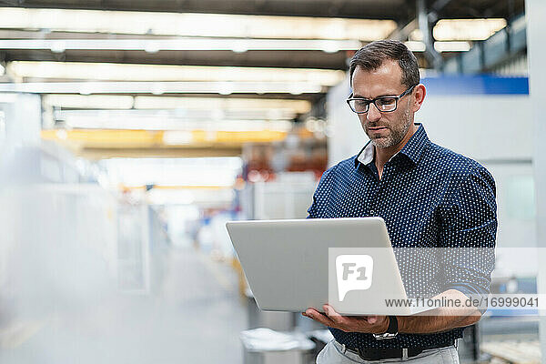 Geschäftsmann  der konzentriert an einem Laptop in einer Fabrik arbeitet