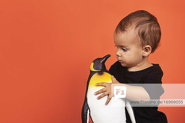 Baby-Mädchen spielt mit Pinguin Spielzeug  während gegen orange Hintergrund sitzen