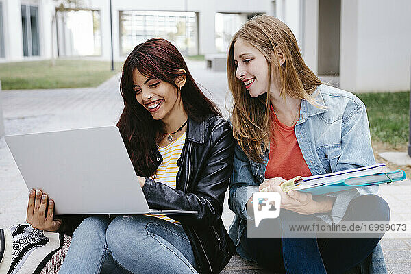 Young female students smiling while using laptop at campus
