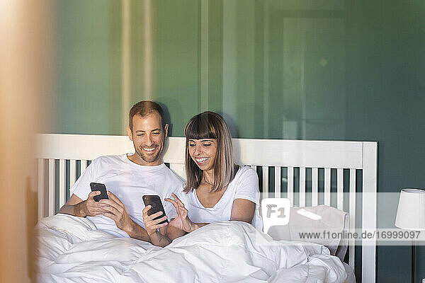 Mittleres erwachsenes Paar lächelt bei der Benutzung eines Mobiltelefons zu Hause