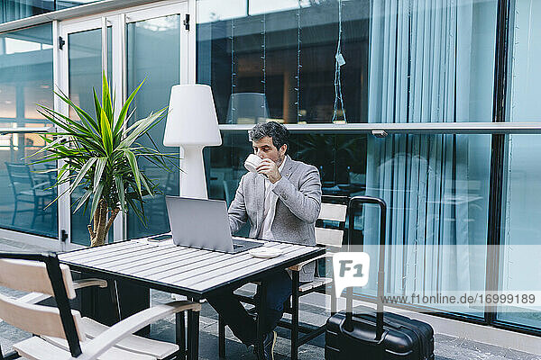 Älterer Geschäftsmann  der einen Laptop benutzt  während er in einem Café Kaffee trinkt
