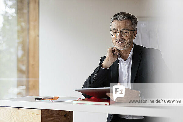 Smiling businessman with hand on chin using digital tablet at home