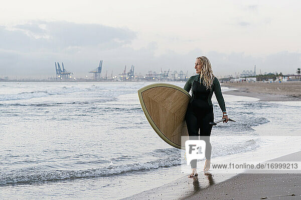 Blonde Frau mit Paddleboard am Strand in der Morgendämmerung