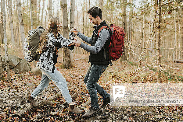 Junger Mann hilft seiner Freundin bei einer Wanderung im Herbstwald
