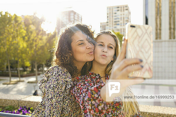 Weibliche Freunde knutschen  während sie ein Selfie durch ein Smartphone an einem sonnigen Tag machen
