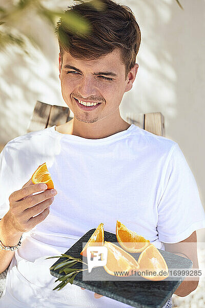 Smiling young man holding marble tray with slice of oranges against wall