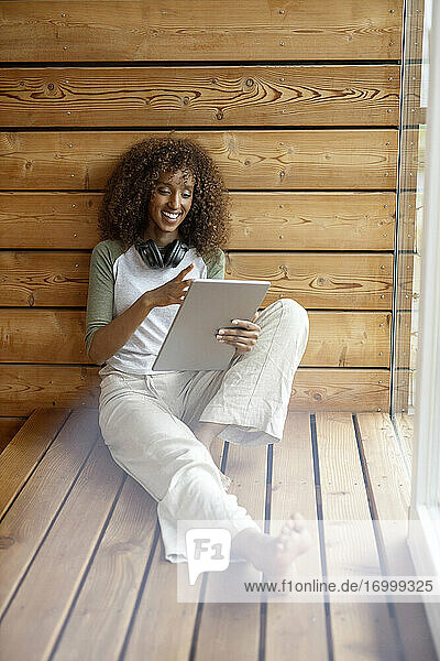 Junge Frau lächelt  während sie zu Hause sitzend ein digitales Tablet benutzt