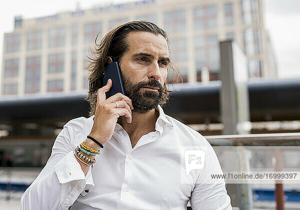 Candid portrait of bearded businessman sitting outdoors and talking on smart phone