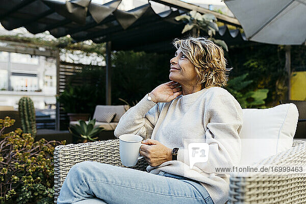 Lächelnde Frau  die mit einer Kaffeetasse in der Hand auf dem Dach sitzt und wegschaut