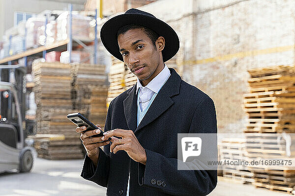 Fashionable man with cool attitude holding mobile phone in wood plallets warehouse