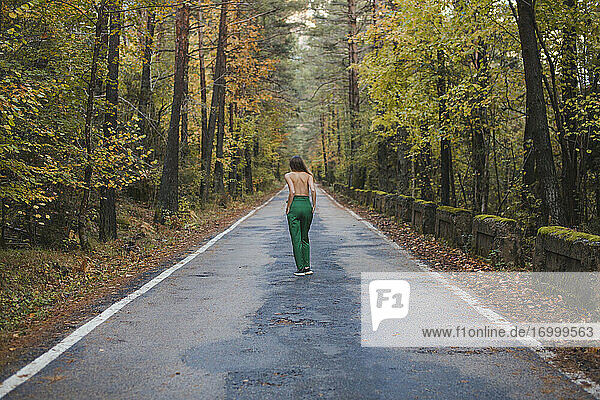 Rückansicht einer jungen Frau ohne Hemd  die auf einer Landstraße steht