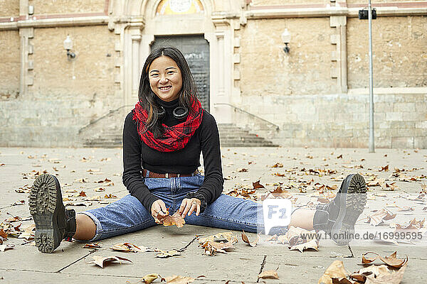 Lächelnde Frau  die auf dem Fußweg sitzend mit einem heruntergefallenen trockenen Blatt spielt