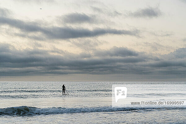 Frau Paddleboarding auf dem Meer gegen den Himmel in der Morgendämmerung