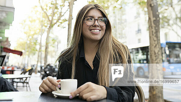 Junge Frau mit Kaffeetasse  die lächelnd in einem Straßencafé in der Stadt sitzt