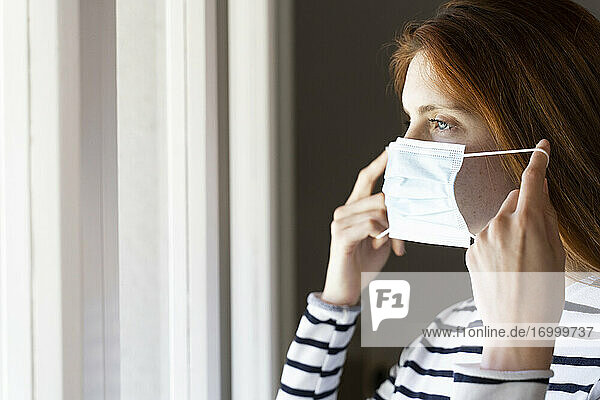 Young woman wearing protective face mask while standing at home during COVID-19