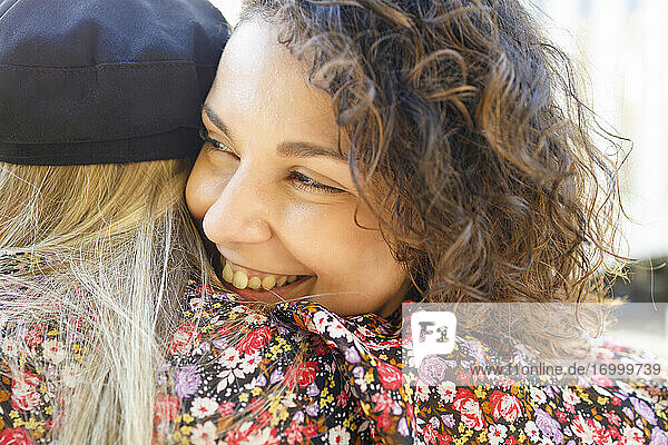 Lächelnde Freundin umarmt blonde Frau an einem sonnigen Tag