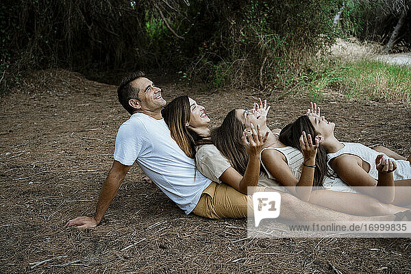Cheerful family doing yoga while lying down in row at forest during vacation