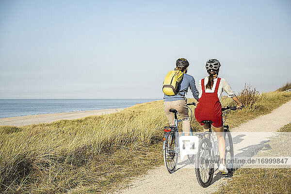 Young couple wearing cycling helmet riding bicycles against clear sky