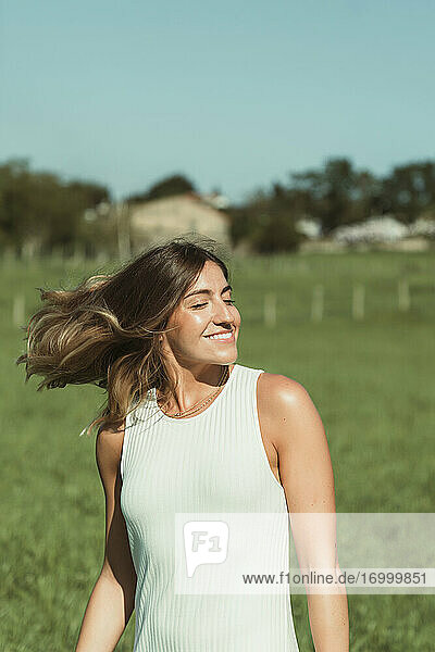 Junge Frau  die sich die Haare wirft  während sie im Park an einem sonnigen Tag steht