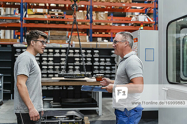 Mature male technician discussing with young coworker in factory