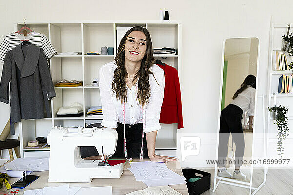 Creative female tailor leaning on desk in studio