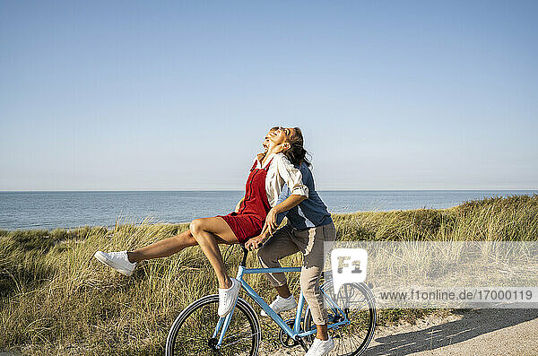 Happy girlfriend sitting on handle while enjoying bicycle ride with boyfriend against clear sky