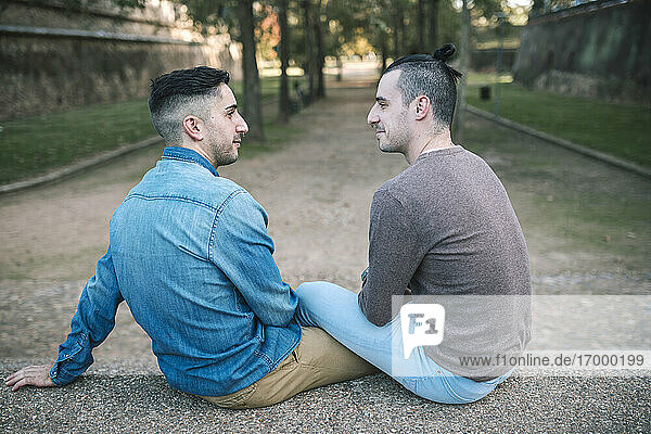 Homosexual couple looking at each other while sitting on footpath in public park