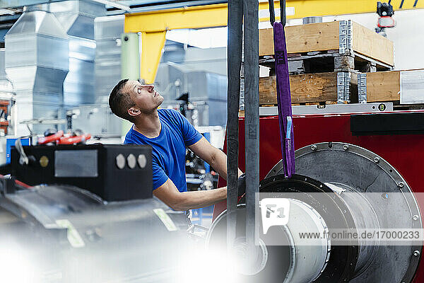 Männlicher Arbeiter  der nach oben schaut  während er an einer Maschine in der Industrie steht