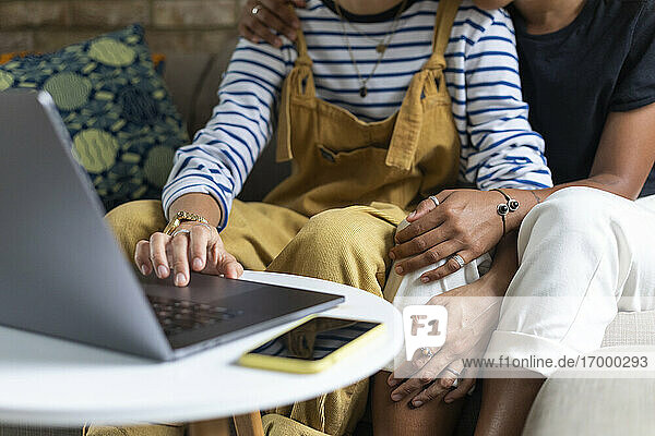 Lesbisches Paar  das einen Laptop benutzt  während es zusammen zu Hause auf dem Sofa sitzt