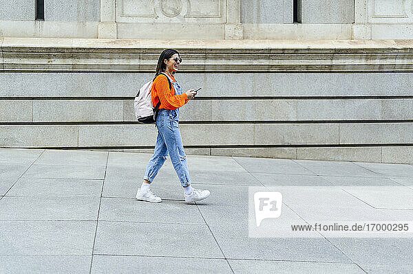 Frau mit Rucksack und Mobiltelefon lächelnd auf dem Fußweg