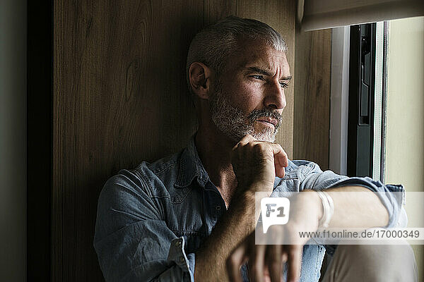 Handsome mature man contemplation while looking through window at home