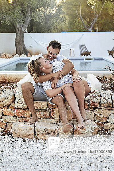 Glückliches junges Paar  das sich anschaut  während es am Swimmingpool im Hinterhof sitzt