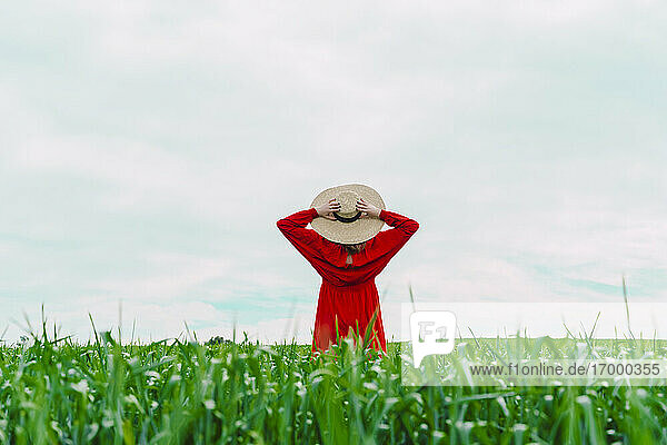 Frau in rotem Kleid und Strohhut auf einem Feld stehend
