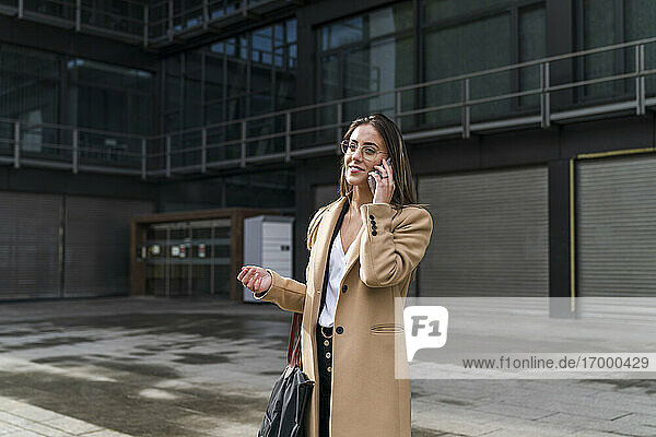 Smiling businesswoman talking on phone against office building