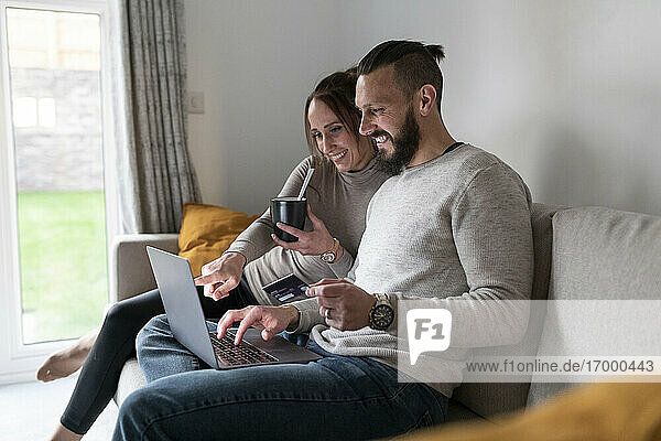 Smiling couple online shopping through laptop while having tea at home