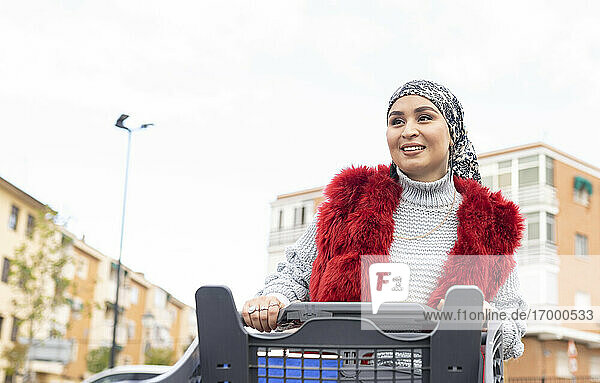 Young woman standing with shopping cart at city