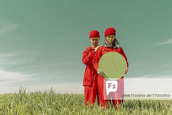 Young couple wearing red overalls and hats standing on a field with green circle