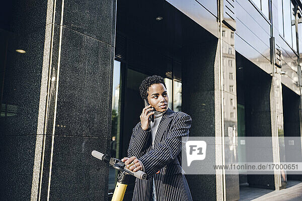 Young businesswoman with electric push scooter looking away while talking through mobile phone