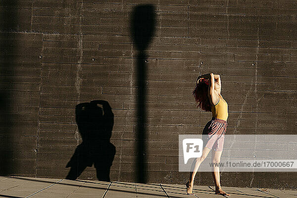 Tanzende junge Frau  die bei Sonnenuntergang Schatten auf eine schwarze Wand wirft