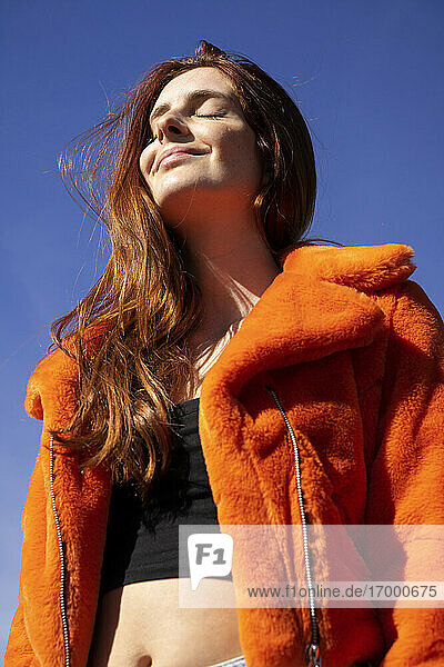 Smiling woman with eyes closed standing against clear sky