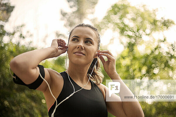 Sportlerin stellt In-Ear-Kopfhörer ein  während sie im Freien steht