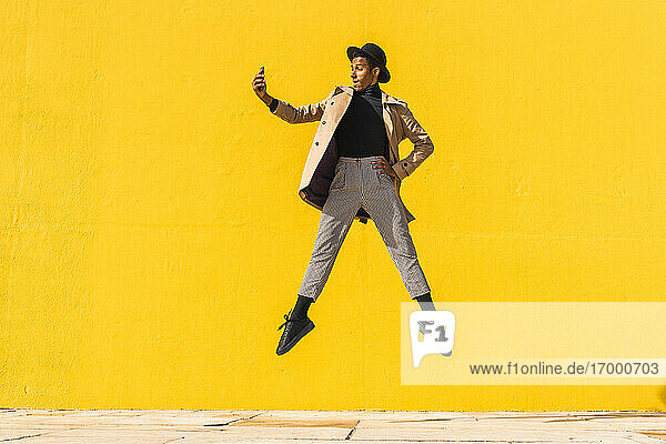 Junger Mann tanzt vor einer gelben Wand und macht Selfies
