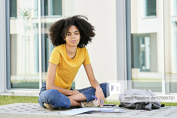 Student mit Buch  der auf dem Universitätscampus sitzt und studiert