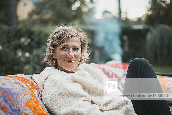 Lächelnde Frau  die sich auf dem Sofa im Hinterhof entspannt