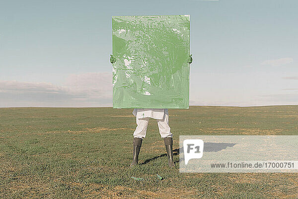 Junge Frau versteckt sich hinter grünem Gemälde auf trockenem Feld