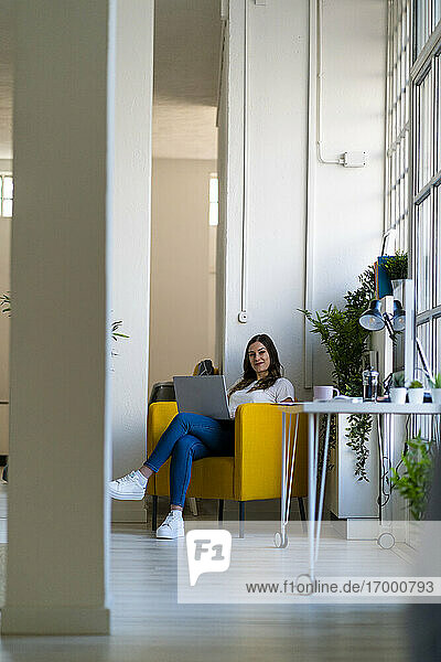 Geschäftsfrau mit Laptop auf einem Sessel im Büro sitzend