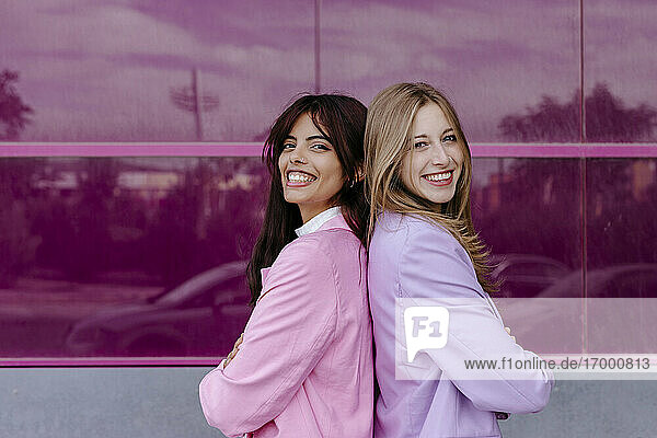 Lächelnde Schwestern stehen Rücken an Rücken vor einer Acrylglaswand