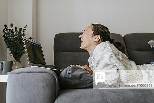 Woman laughing while talking to friend through video call on laptop at home